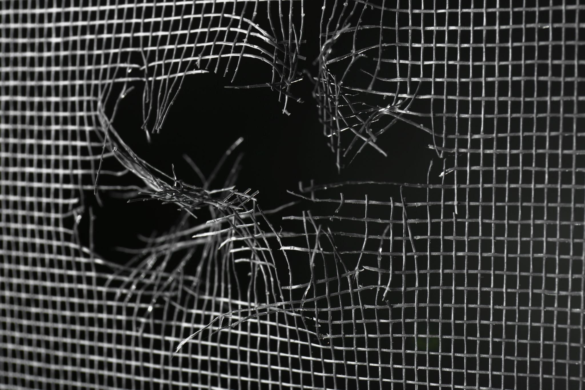 Torn window screen against black background, closeup